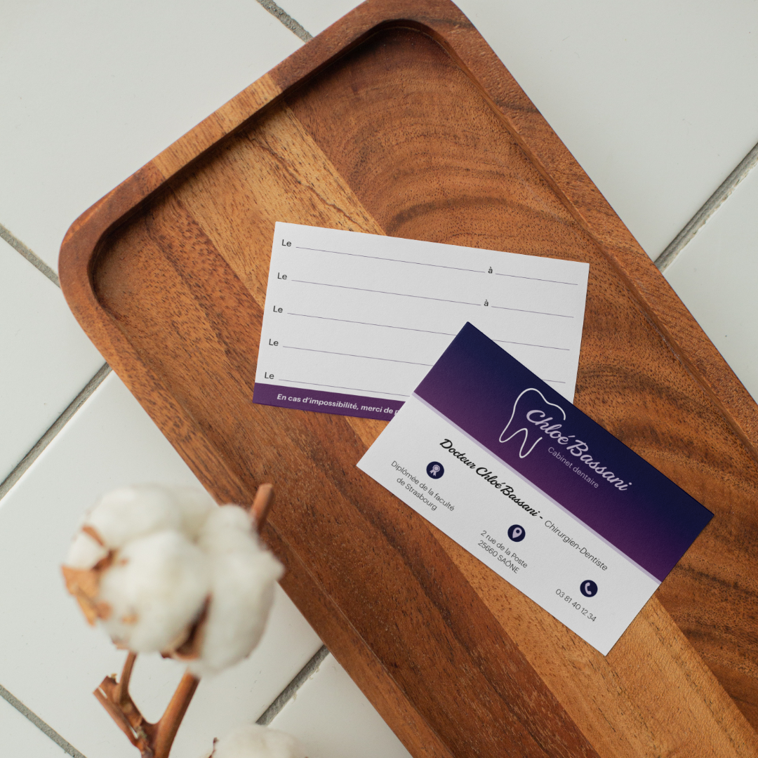 Cartes de visite créées par l'agence de communication Okami pour le cabinet dentaire Chloé Bassani. Le recto est divisé en deux parties : en haut, le logo sur fond violet dégradé, et en bas, le nom et la fonction et les coordonnées sont présentes. Au verso, sur un fond blanc, des lignes permettant de noter des rendez-vous sont présentes.