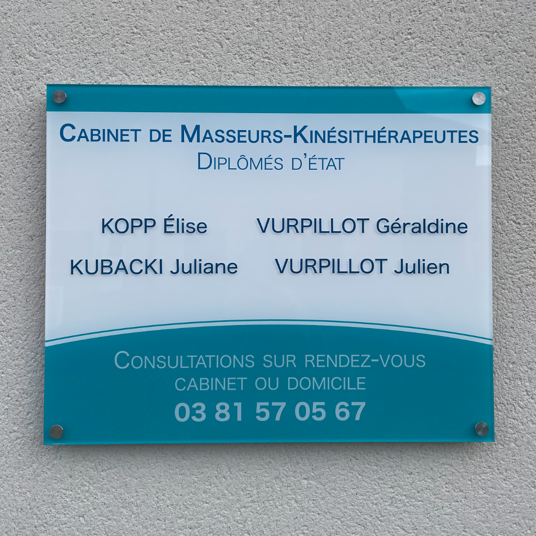 Plaque de cabinet de kinésithérapeute accrochée sur un mur, créée par l'agence de communication Okami. La plaque possède une bande bleue tout en haut. En dessous, "Cabinet de Masseurs-Kinasithérapeutes" et les noms des praticiens sont inscrits en bleu foncé sur fond blanc. En dessous, sur un fond bleu clair arrondi est inscrit le numéro de téléphone.
