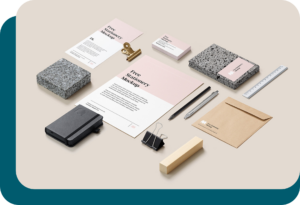 Différents types de supports de communication (carte de visite, flyer, plaquette, enveloppe personnalisée...) positionnés de manière harmonieuse avec un stylo, un crayon, un carnet, des pinces et une règle, sur un fond beige. Tous les supports sont harmonisés au niveau du graphisme.