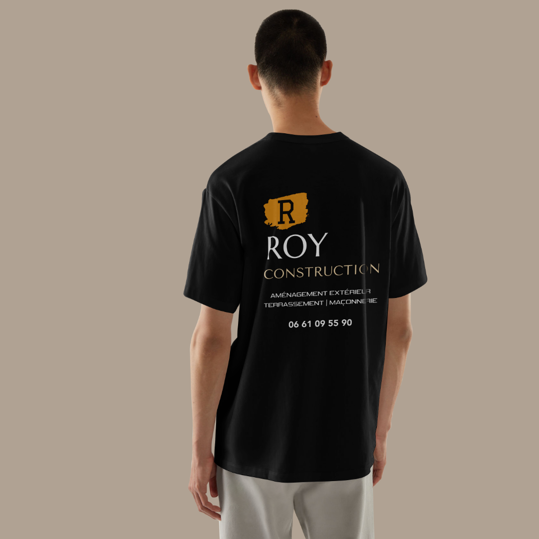 Homme de dos portant un t-shirt noir floqué par l'agence de communication Okami pour l'entreprise Roy Construction. Sur le dos du t-shirt, le logo est en haut et centré, en dessous les services "aménagement extérieur", "terrassement" et "maçonnerie" sont inscrits et le numéro de téléphone est présent en dessous.