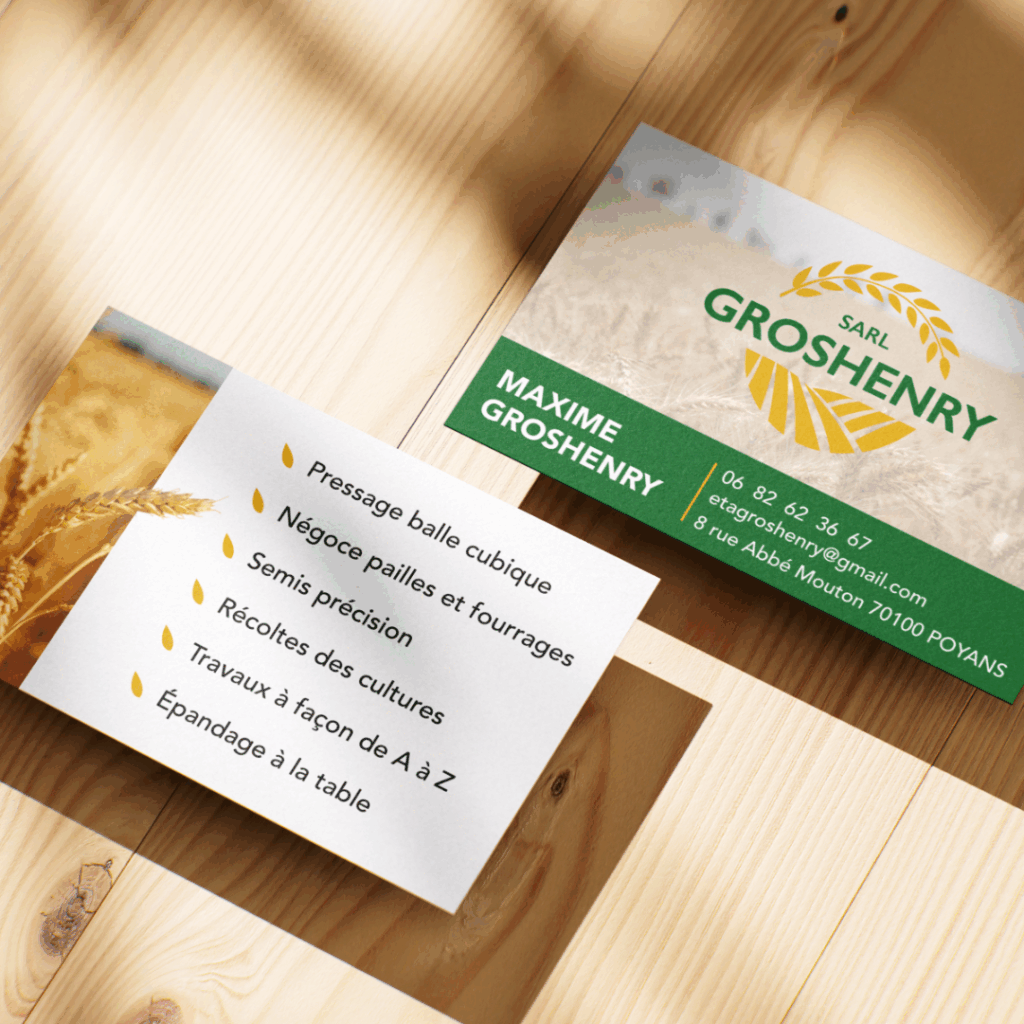 Photographie de deux cartes de visite posées sur une surface en bois clair. La première carte, au recto, présente le logo jaune en forme d’épi de blé de la SARL Groshenry avec un fond de champ de blé, le nom “Maxime Groshenry” sur un bandeau vert, ainsi que les coordonnées : numéro de téléphone, adresse e-mail et adresse postale à Poyans. La seconde carte, au verso, affiche une photo de blé à gauche et une liste de services agricoles à droite, tels que pressage balle cubique, négoce pailles et fourrages, semis précision, récoltes de cultures, travaux à façon et épandage à la table.